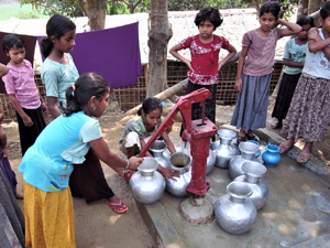 小学生くらいの女の子たち10名近くが井戸を囲む　1人の少女が井戸のポンプを押している