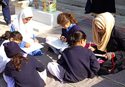子どもたちが青空のもと、広場にシートを敷いて熱心に絵を描いている。