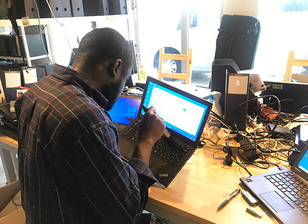 パソコンの整備をしている男性の後ろ姿　パソコンの備品などがデスク周辺にたくさん置かれている