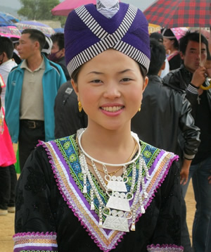 10代くらいの女性が、紫色の帽子をかぶっている。首には銀色のアクセサリーを付けている。服の方から胸元にかけては、緑や紫色の刺繍がほどこされている
