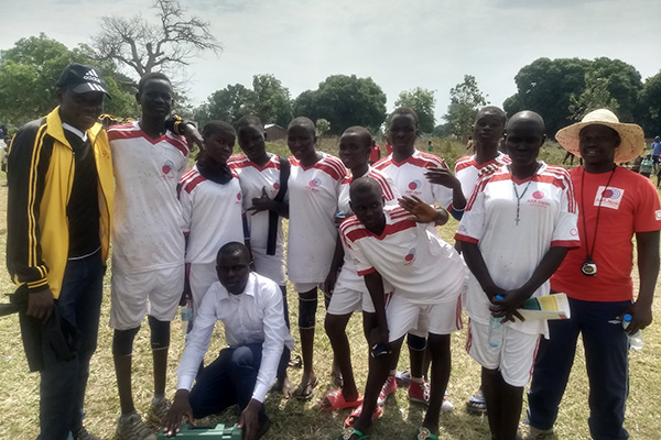 AARスタッフや生徒10人ほどと一緒にカメラに向かい微笑むジョエル先生