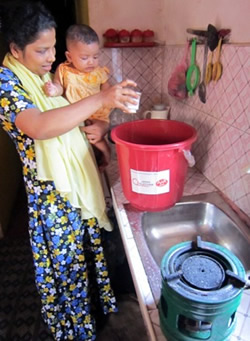 息子を抱いて、バケツとコンロを使うシッティさん