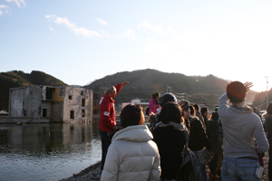 横倒しになったビルの残る被災地を見学する皆様