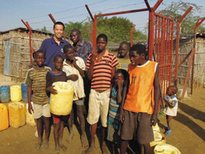 柵に囲われた水栓所の前で、子どもたちと池田駐在員