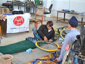 床に座って車いすの車輪を組み立てるディルショッドさん