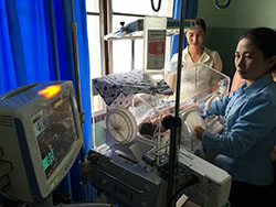 保育器に入った赤ちゃんを見ているふたりの女性