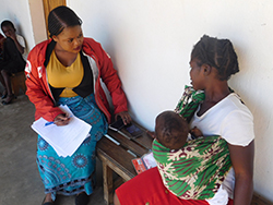 赤ちゃんを抱えて座る女性に話をきくセシリア