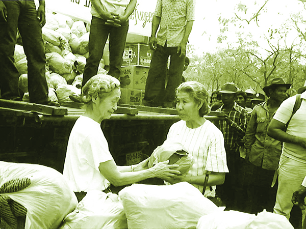 支援物資を積んだトラックの前で女性の難民の方に袋を相馬が手渡している