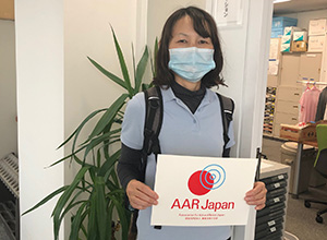 支援物資を受け取った日本訪問介護財団様の助成が、AARのロゴが書いてある紙を持って立っている