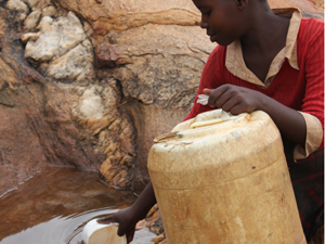 ケニア、キツイ県ムトモ郡で岩場に溜まった雨水を汲む少女
