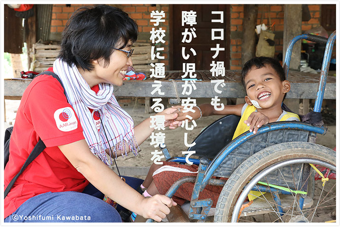 カンボジアの支援現場で、車いすに乗った障がい児が笑顔でAAR職員と手をつないでいる　AAR職員は腰をおろし、障がい児と同じ目線に立っている